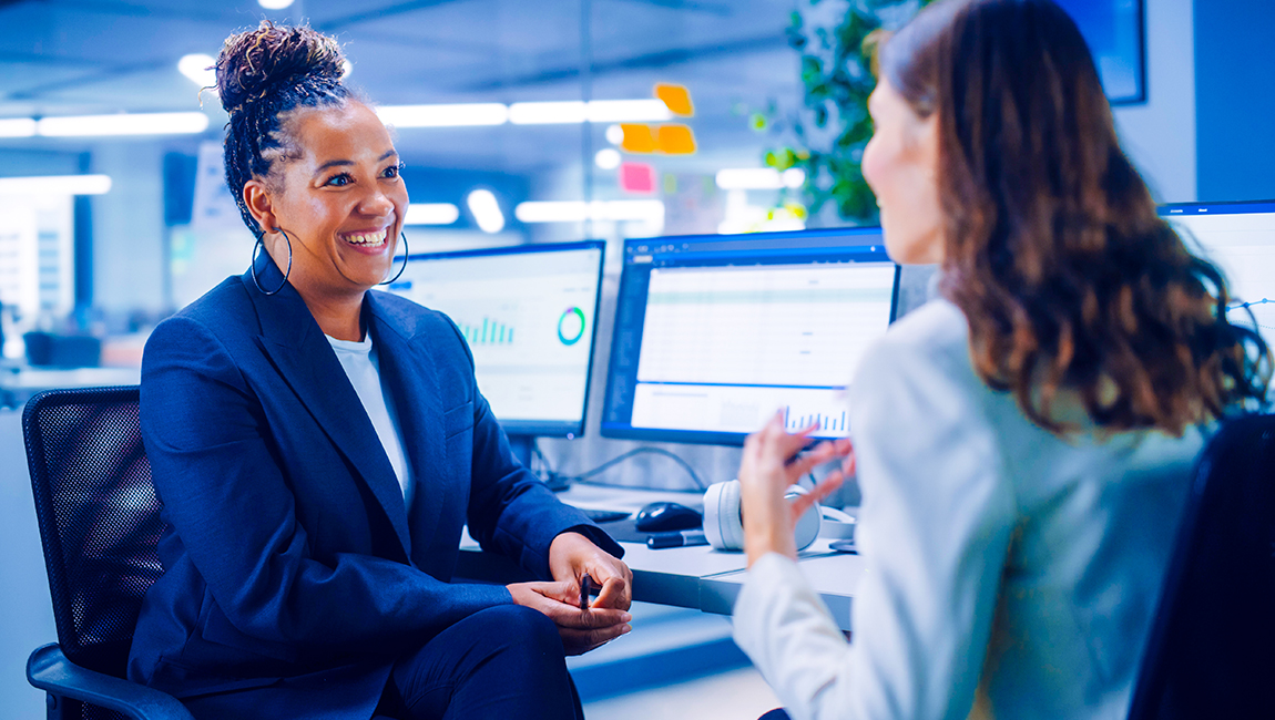 Two female colleagues having a discussion while at their desks