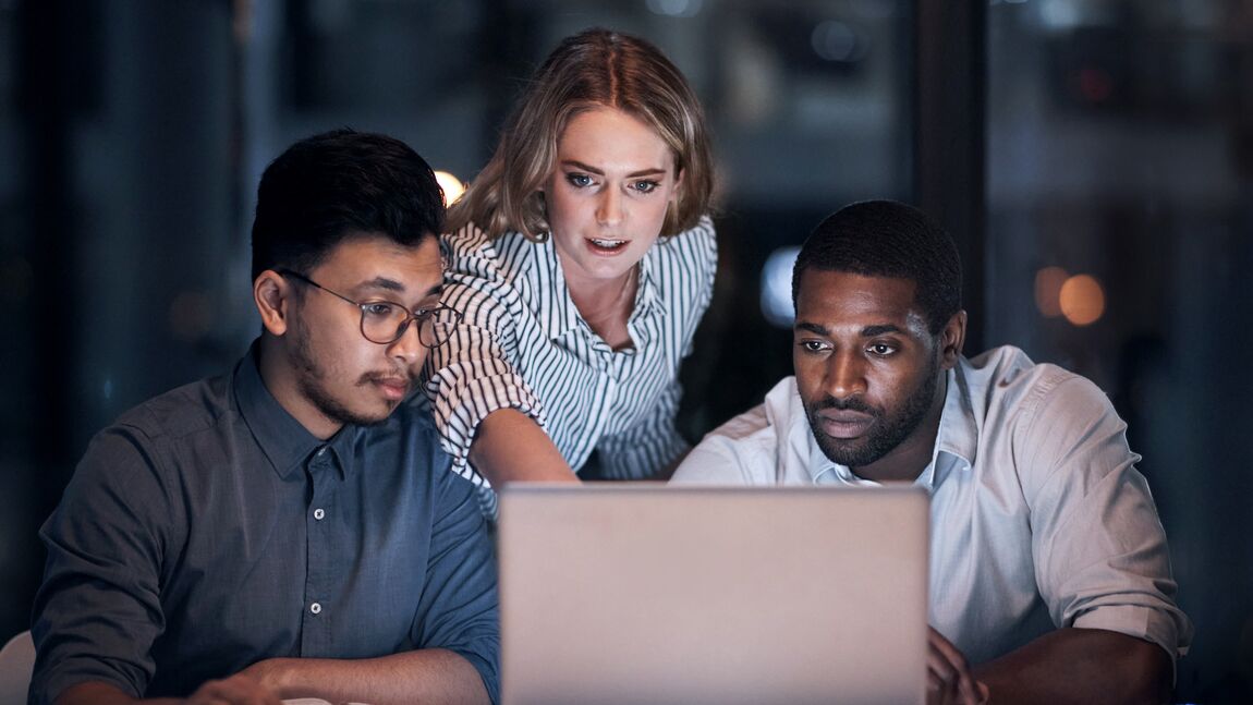 Team of colleagues looking at laptop in office at night