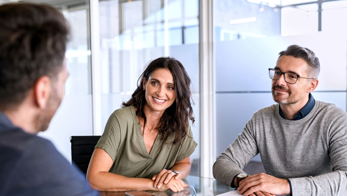 Three colleagues smiling around glass table in modern office