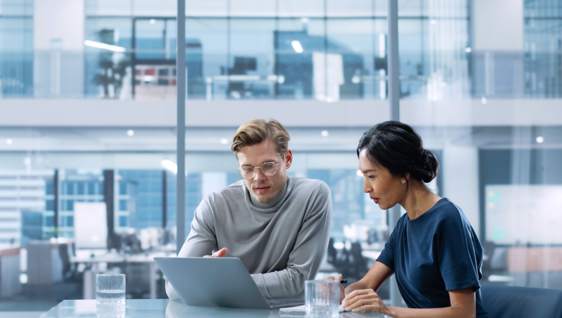 Two colleagues in a modern office looking at a laptop together