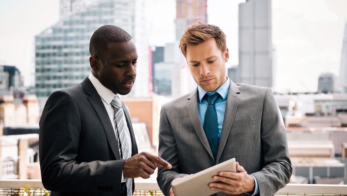 Two male colleagues looking at tablet while standing outside on office terrace