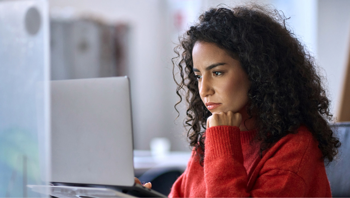 Woman wearing red sweater studying laptop screen