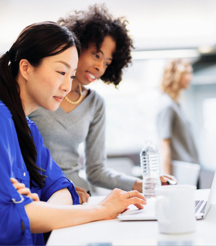 Two businesswomen looking at laptop in bright office space