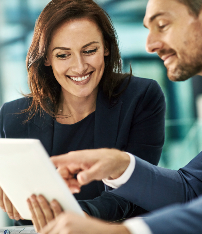Two colleagues smiling looking and pointing at tablet